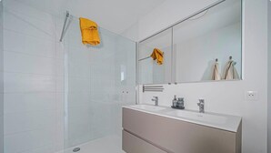 Une salle de bain moderne avec une douche à l’italienne en verre, un meuble-lavabo blanc doté de deux vasques et un grand miroir.