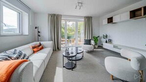 Un salon moderne comprenant un canapé, des fauteuils, une table basse et une vue sur un espace extérieur, accessible par une porte vitrée.