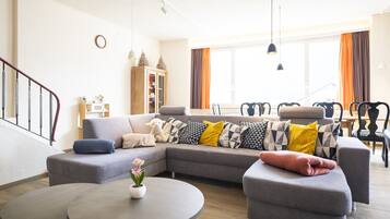 Ein modernes Wohnzimmer mit einem grauen Ecksofa, einem kleinen runden Tisch und einer Treppe.