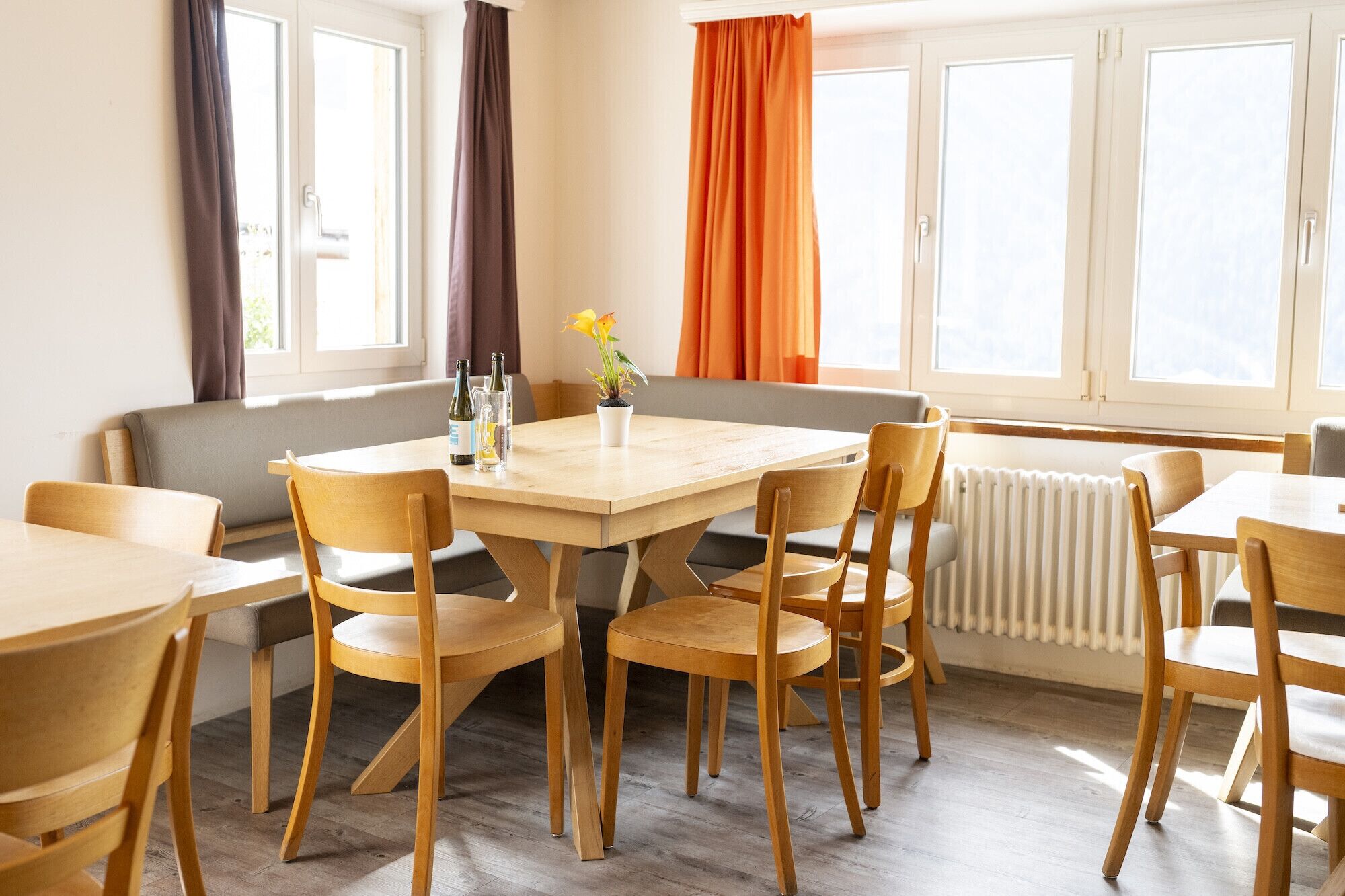 Un espace repas avec des tables et des chaises en bois, un banc et une fenêtre avec des rideaux.