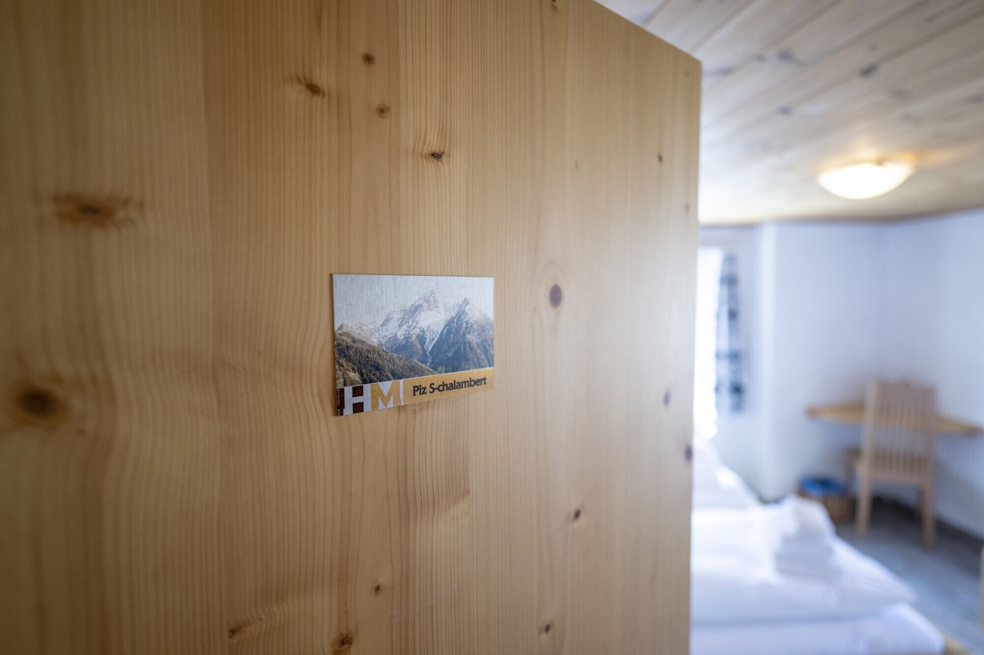 Eine Holzwand mit einem kleinen Schild, auf dem 'HM Piz Schalambert' steht.