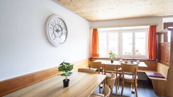 Ein Essbereich mit einem Holztisch und Stühlen, einer Uhr an der Wand und einem Fenster mit Vorhängen.