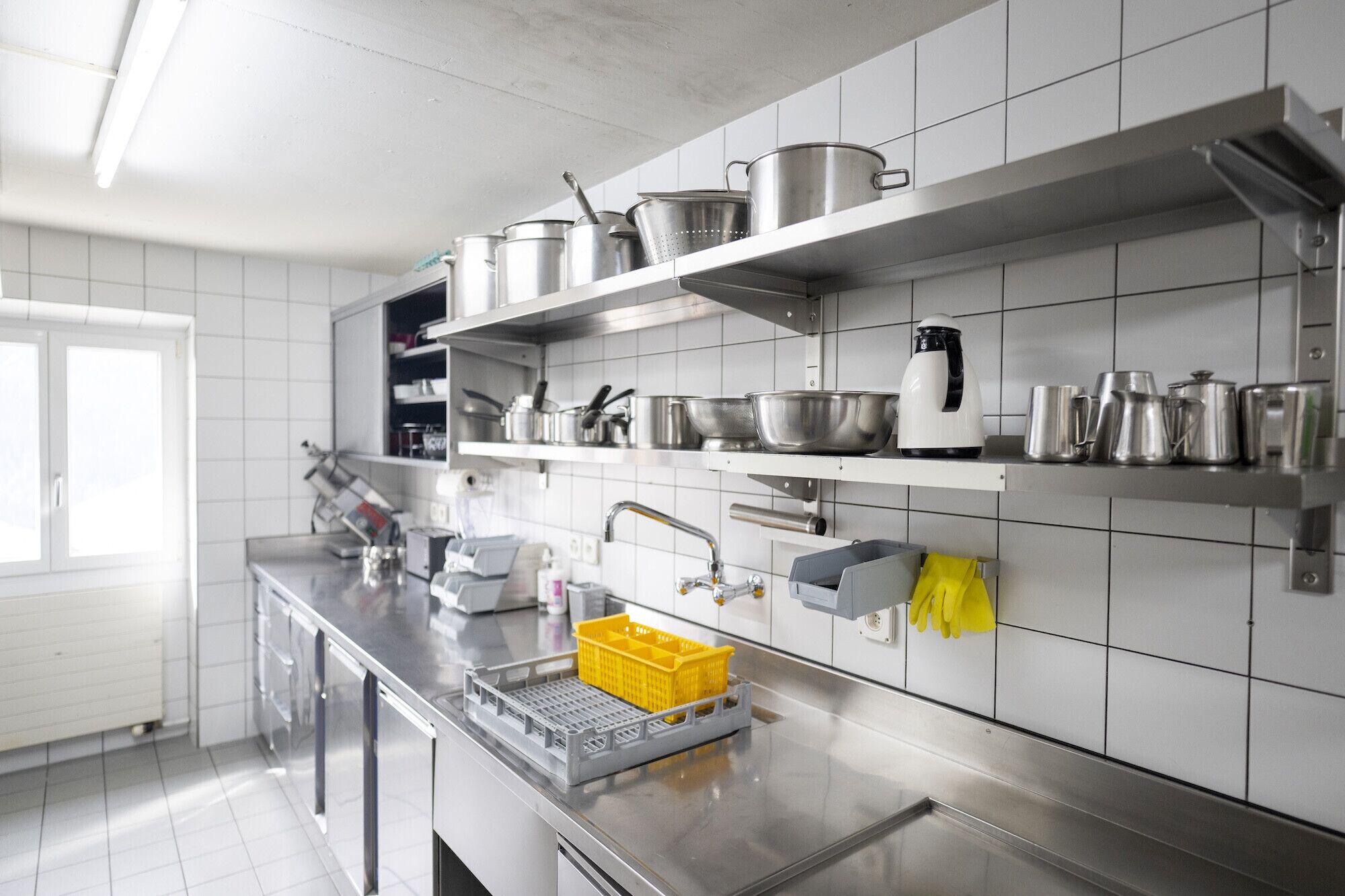 Une cuisine moderne dotée d’appareils électroménagers en acier inoxydable, de murs recouverts de carreaux blancs et d’une variété d’ustensiles de cuisine rangés sur des étagères.