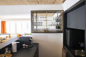 A modern kitchen with a built-in glass display cabinet for dinnerware, a coffee machine, and a stainless steel refrigerator.
