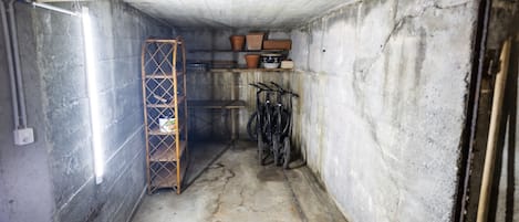 Un pasillo estrecho y poco iluminado, con suelo de hormigón, un estante de metal y una bicicleta apoyada en la pared.
