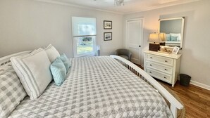 Een slaapkamer met een bed, een plafondventilator, een raam, een deur, een dressoir en een spiegel.