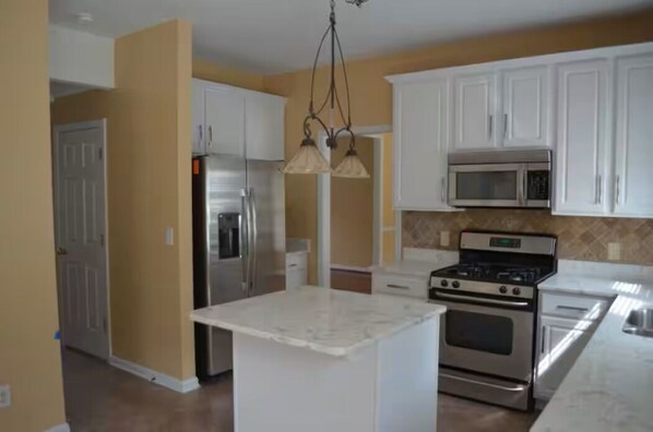 A kitchen with white cabinets, stainless steel appliances, and a marble island.