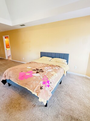 A bedroom with a bed, carpeted floor, and a door leading to another room.