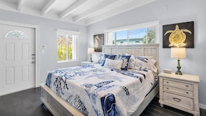 Ein Schlafzimmer mit Bett, Nachttischen, einer Kommode, einem Deckenventilator und Kunstwerken an den Wänden.
