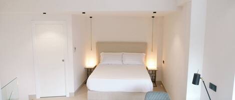 A bedroom with a bed, bedside lamps, a glass table, and a chair.