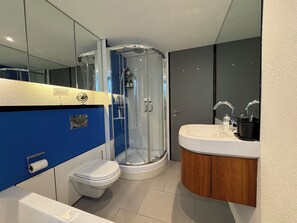Et moderne badeværelse med et glasafskærmet brusebad, et hvidt toilet, en vask med et spejl og en blå væg.