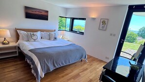 A bedroom with a bed, bedside tables, a chair, a desk, and a view of greenery through a window. - The Seahorse Torbay - Seaside hideaway for two with hot tub and movie room (Torquay)