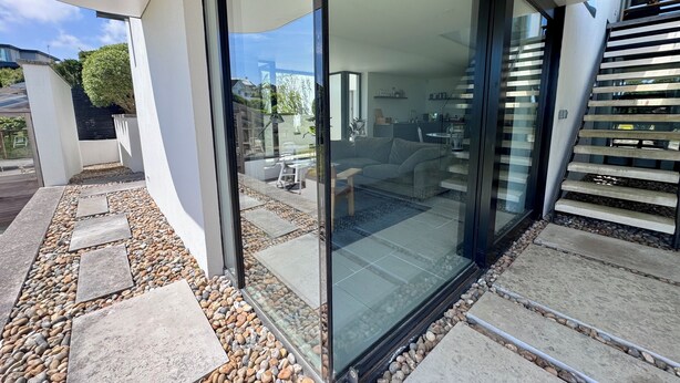 A modern house with a glass door leading to a living area, a stone pathway, and a staircase. - The Seahorse Torbay - Seaside hideaway for two with hot tub and movie room (Torquay)