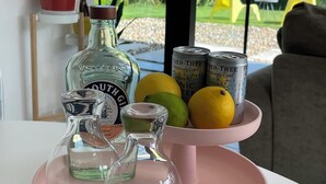 A table with a pink tray holding a bottle, a glass, and two cans, with lemons and a potted plant in the background. - The Seahorse Torbay - Seaside hideaway for two with hot tub and movie room (Torquay)