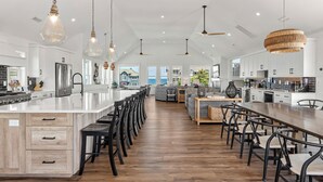Een ruime keuken met een groot eiland, moderne apparatuur en hanglampen.