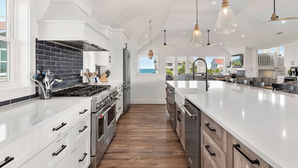 Een moderne keuken met witte kasten, een zwart betegelde spatwand, roestvrijstalen apparatuur en hanglampen.