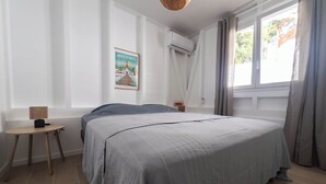 Camera da letto con un letto, un tavolino, condizionatore d'aria a parete e una finestra con tende.