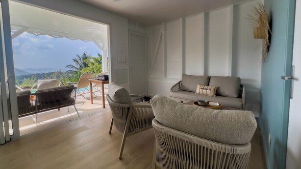 Un soggiorno moderno con divano, poltrone, una ventola a soffitto e vista sull'esterno.