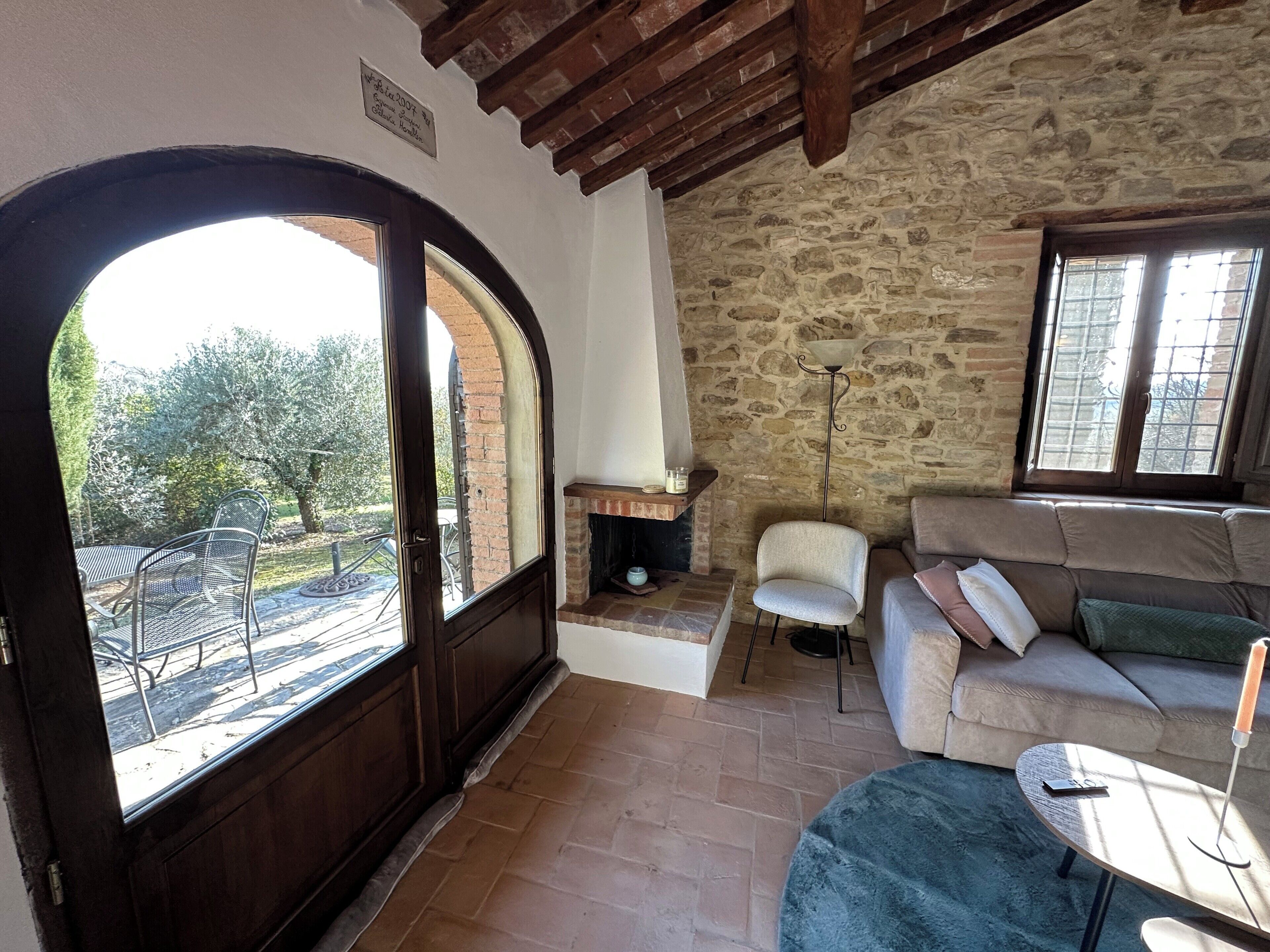 A room with a stone wall, a fireplace, a sofa, a table, and a door leading to an outdoor area.