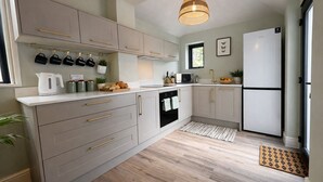 Una cocina moderna con lavavajillas integrado, microondas y refrigerador. Hay armarios con tiradores dorados, un colgador para ollas y una ventana que proporciona luz natural.