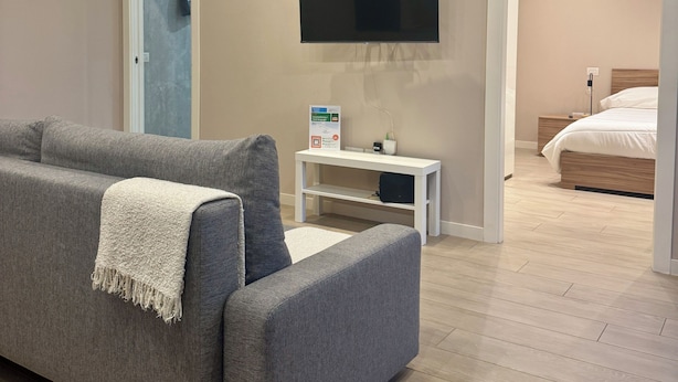 Ett modernt sovrum med en grå soffa, en platt-TV, ett sängbord och en säng av trä.