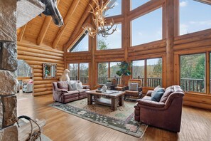 A log cabin interior with a high ceiling, large windows, a fireplace, and a cozy seating area.