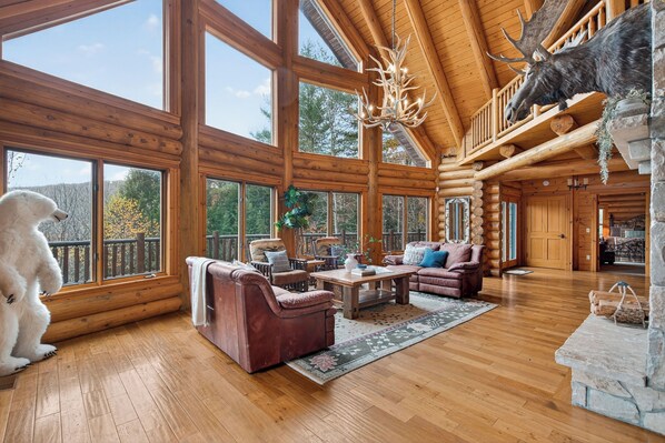 A log cabin interior with large windows, a fireplace, and a mounted moose head.