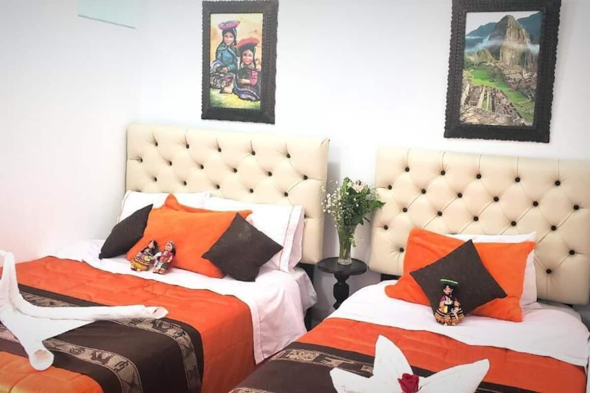 Two beds with tufted headboards, orange and black bedding, and decorative pillows.