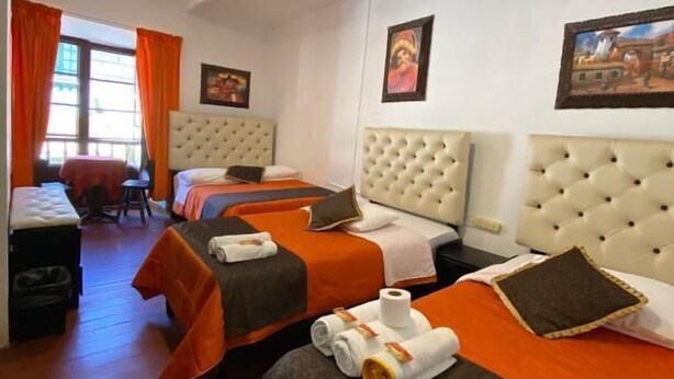 A hotel room with three beds, a dining area, and a window with curtains. - Imperial Golden House Inn (Cusco)