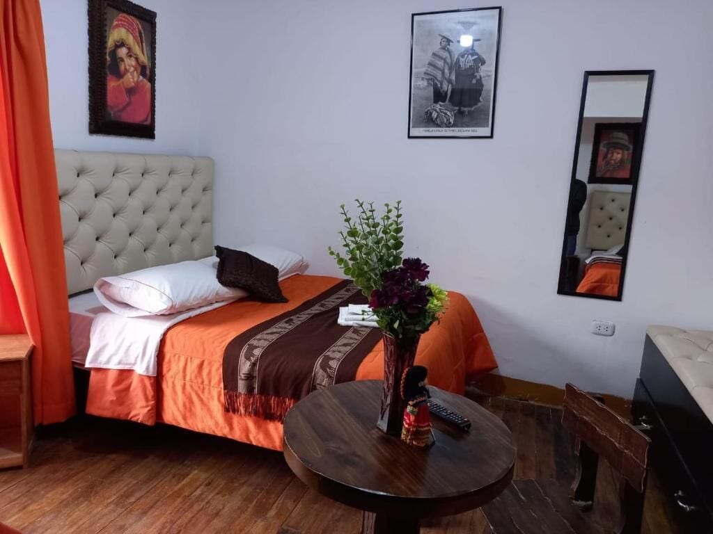 Una habitación de hotel con una cama, una mesa redonda, un florero con flores y un espejo.