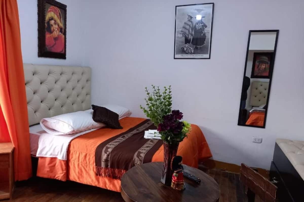 Una habitación de hotel con una cama, una mesa redonda, un florero con flores y un espejo.
