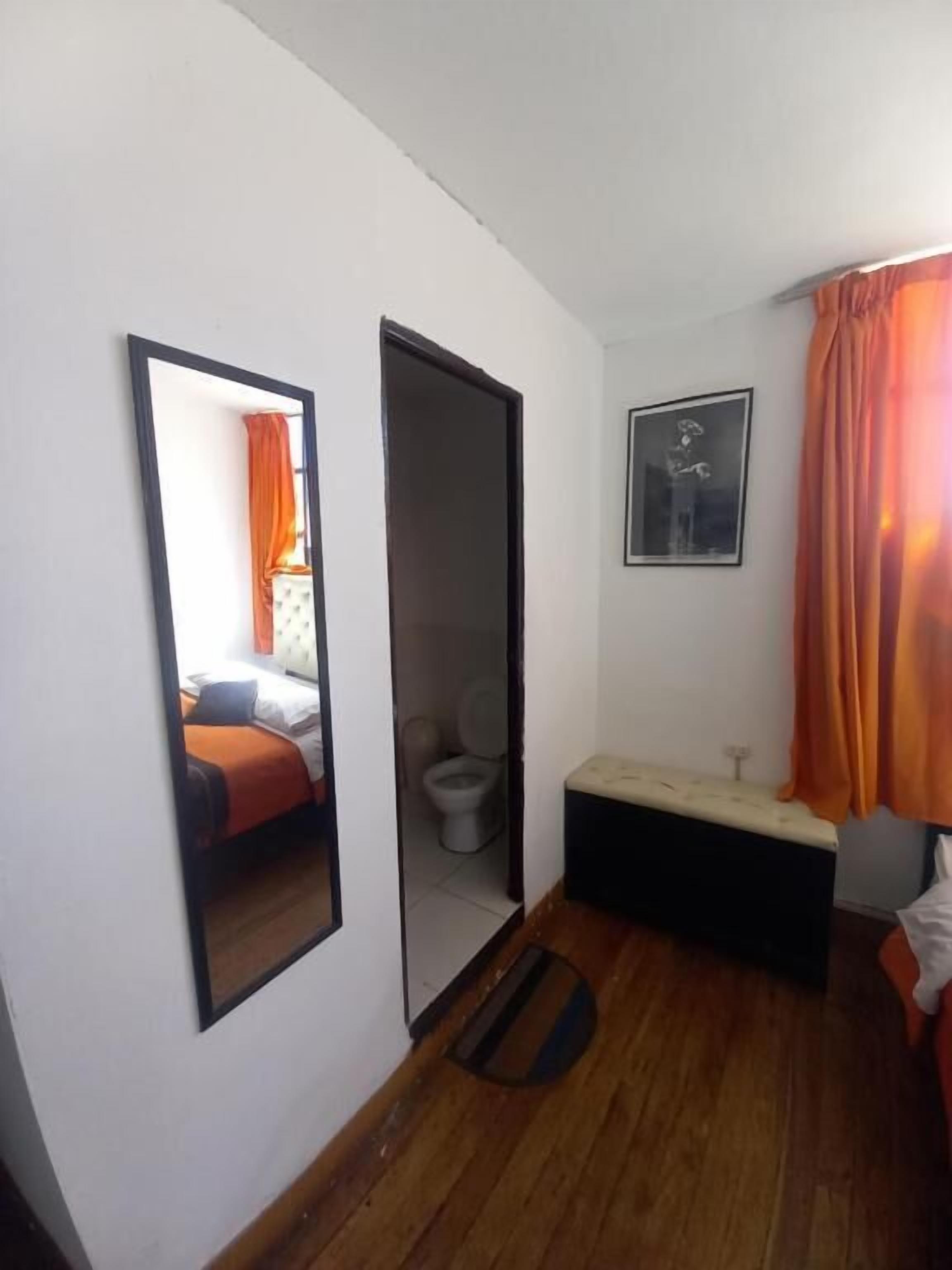 Una habitación con cama, inodoro, banco, espejo y un cuadro en la pared.