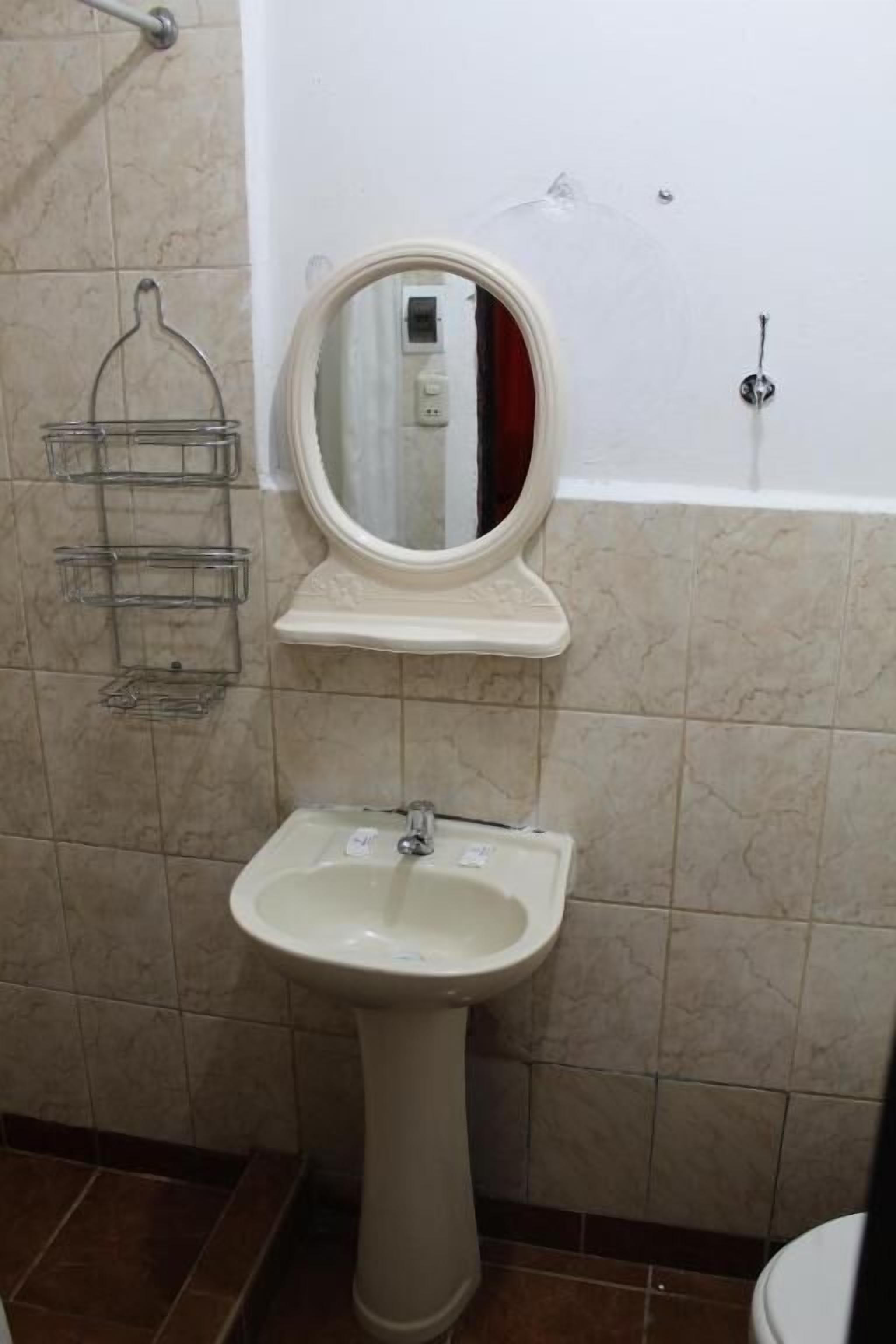 Un baño con lavamanos pedestal, espejo y perchero.