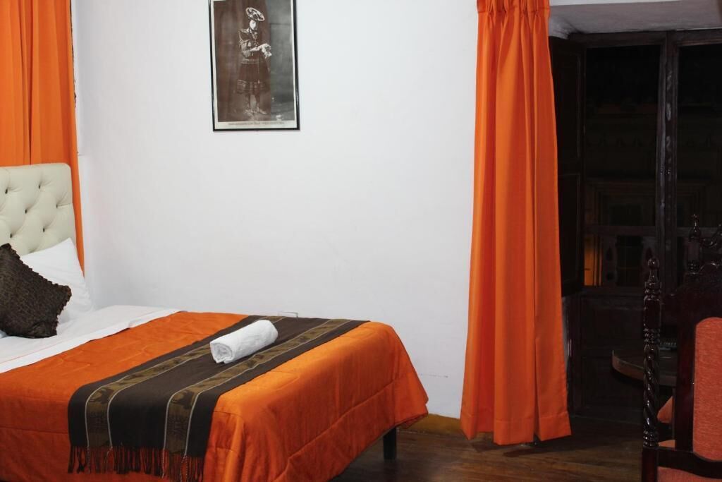 Un lit avec une tête de lit blanche, une couette orange et un tableau encadré accroché au mur.