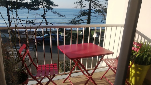 Un balcon avec une table et des chaises rouges, une plante en pot et une vue sur la mer.