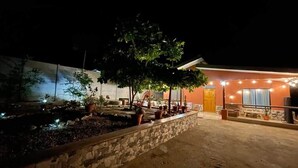 A building with a stone wall, potted plants, and a well-lit entrance. - Casa Neju Diri - surf digital nomad hideaway (Nosara)
