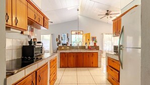 A kitchen with wooden cabinets, a central island, a refrigerator, and a ceiling fan. - Casa Neju Diri - surf digital nomad hideaway (Nosara)