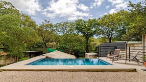 A swimming pool with a surrounding gravel area, a covered structure, and a fenced area with trees. - Casa Neju Diri - surf digital nomad hideaway (Nosara)