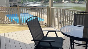 A covered deck with a pool, chairs, and a table overlooking a river and forested hills. - Location Location! Cute cozy condo! Close to everything! (Osage Beach)