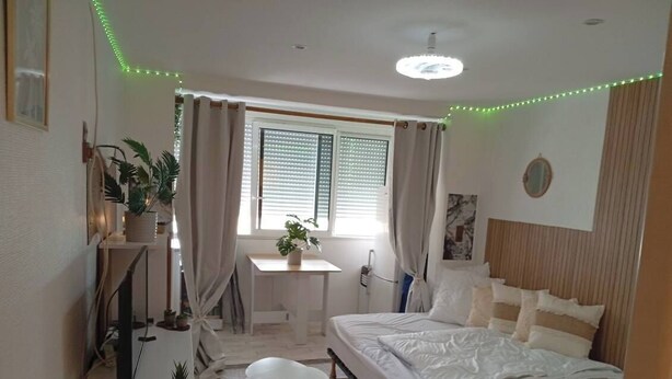 A bedroom with a bed, a desk, a chair, a window with curtains, and a ceiling light. - Magnifique Studio Au Petit Nid Douillet Face Mer est Port (Narbonne)