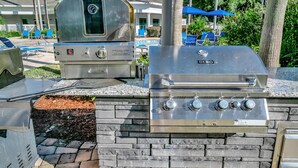 Une cuisine extérieure dotée d’un barbecue intégré et d’un fumoir, le tout installé devant un mur en pierre.