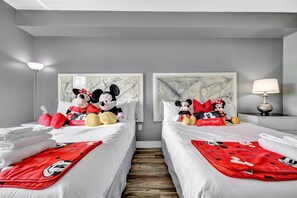 A hotel room with two beds, each with Mickey Mouse-themed bedding and pillows, a marble artwork above the beds, a lamp on the nightstand, and a wooden floor. - 2 Bed Resort Condo NO FEES | Only 8 mins to Disney (Orlando)