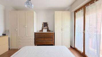 A bedroom with a bed, wooden dresser, white wardrobes, and a hanging light fixture.
