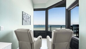 A balcony with two reclining chairs, a white table, and a framed artwork. - 🏝️Sound-Front | Two Balconies | Steps to the Beach | Palm Beach Club #206🏝️ (Pensacola Beach)