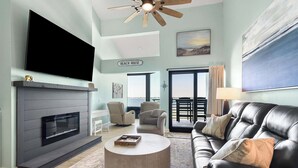 A living room with a fireplace, a flat-screen TV, a leather sofa, and a view of the outdoors. - 🏝️Sound-Front | Two Balconies | Steps to the Beach | Palm Beach Club #206🏝️ (Pensacola Beach)
