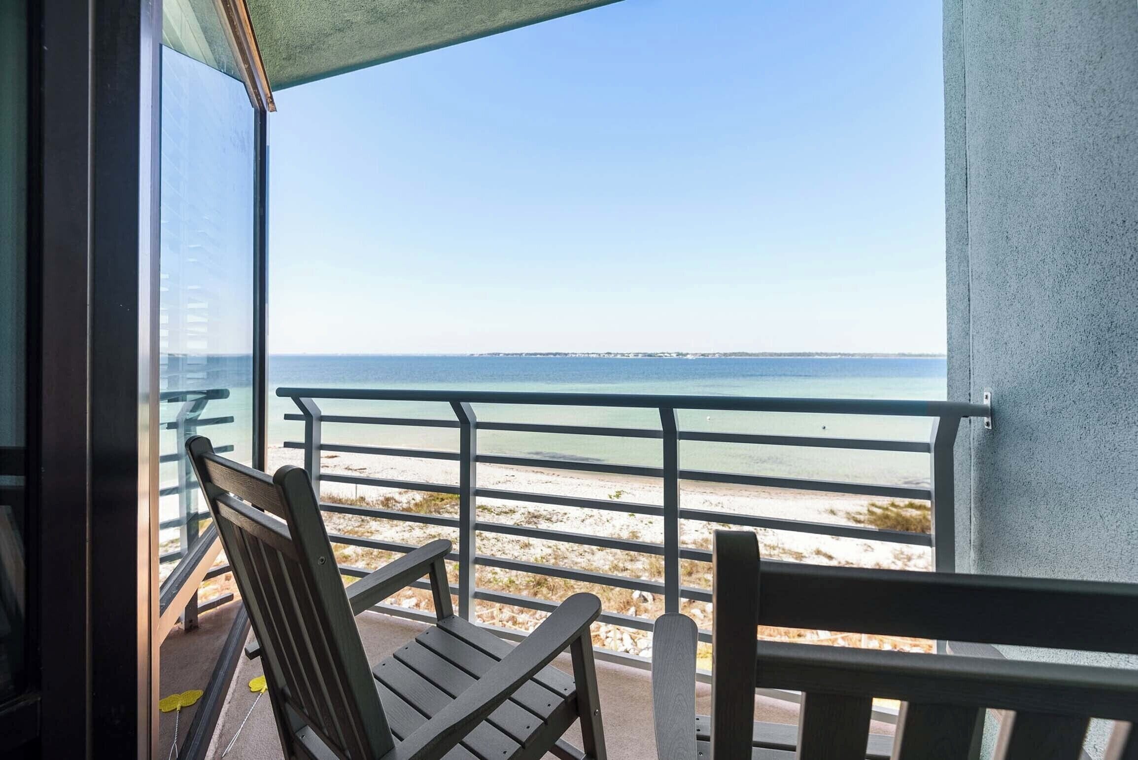 A balcony with a view of the sea, a chair, and a table.