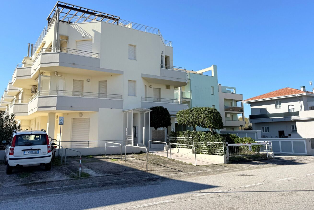 A multi-story residential building with balconies, a gated entrance, and a parked car.
