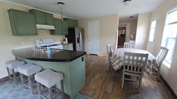 A kitchen with a central island, bar stools, a dining table with a checkered tablecloth, and a refrigerator.