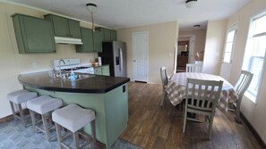 Een keuken met een centraal eiland, barstoelen, een eettafel met een geruit tafelkleed en een koelkast.