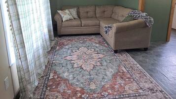 Un salon avec un canapé d’angle, un tapis à motifs, une tête de cerf accrochée au mur et une pancarte portant l’inscription « chez soi ».